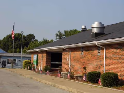 Exterior of River'S Bend Health Care; brick building with flags, shrubs, and a sloped roof.