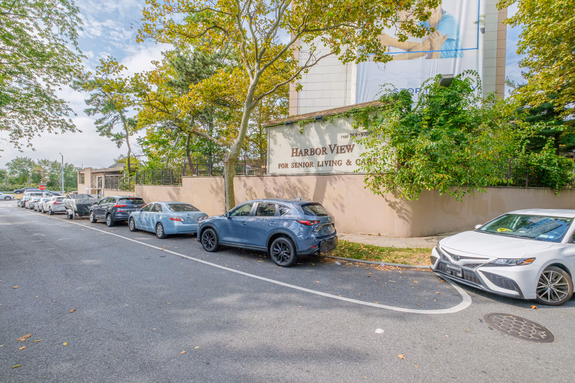 Street-side view of the Harbor View senior living facility sign on a wall with several cars parked along the curb.