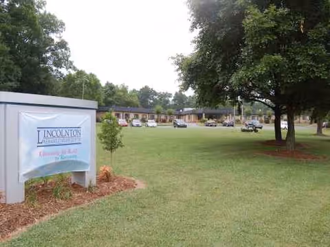 Front exterior of Lincolnton Rehabilitation Center with a grassy lawn and distant single-story buildings.