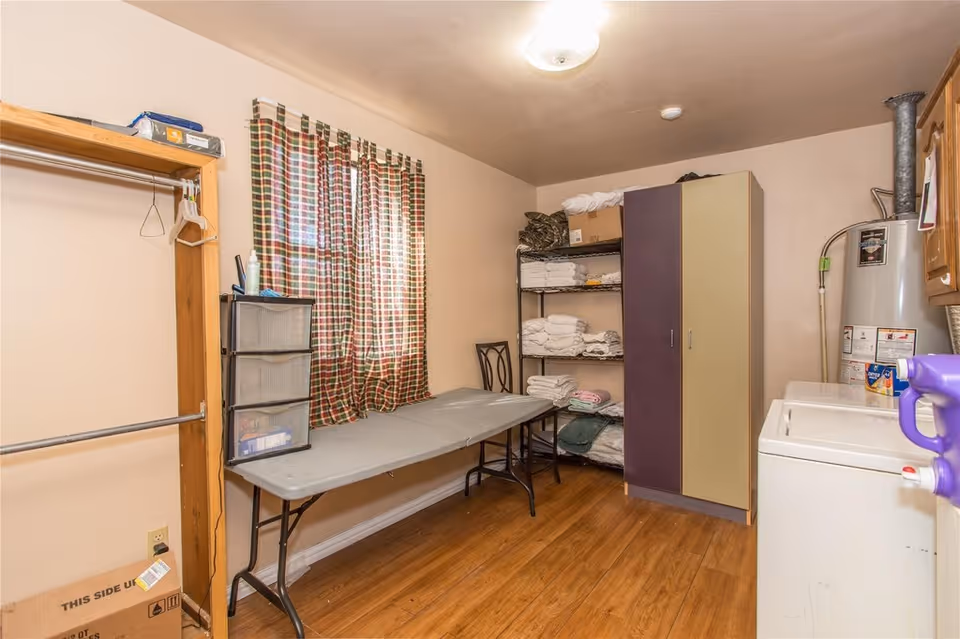 Laundry/storage room with a folding table, shelves of towels, a washer and water heater, and a wardrobe.