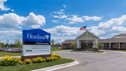 Exterior view of Heartland of Sterling Heights with entrance, flag, and landscaped sign.