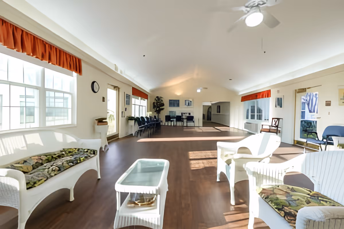 Bright, spacious common sitting room with white wicker chairs, coffee tables, and large windows.
