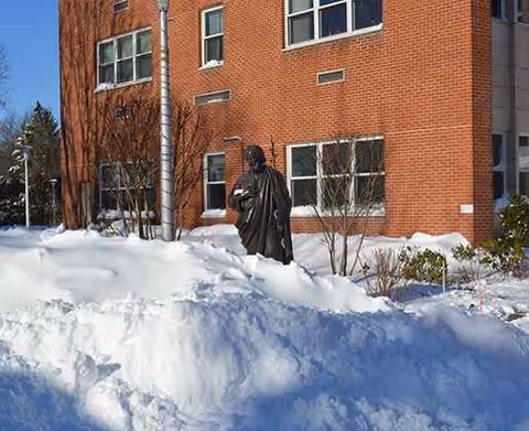 A person walks outside a snow-covered brick building with windows.