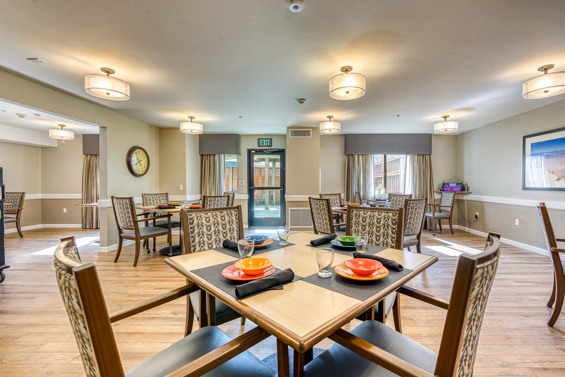 Bright communal dining room with multiple set tables and chairs in a senior living facility.