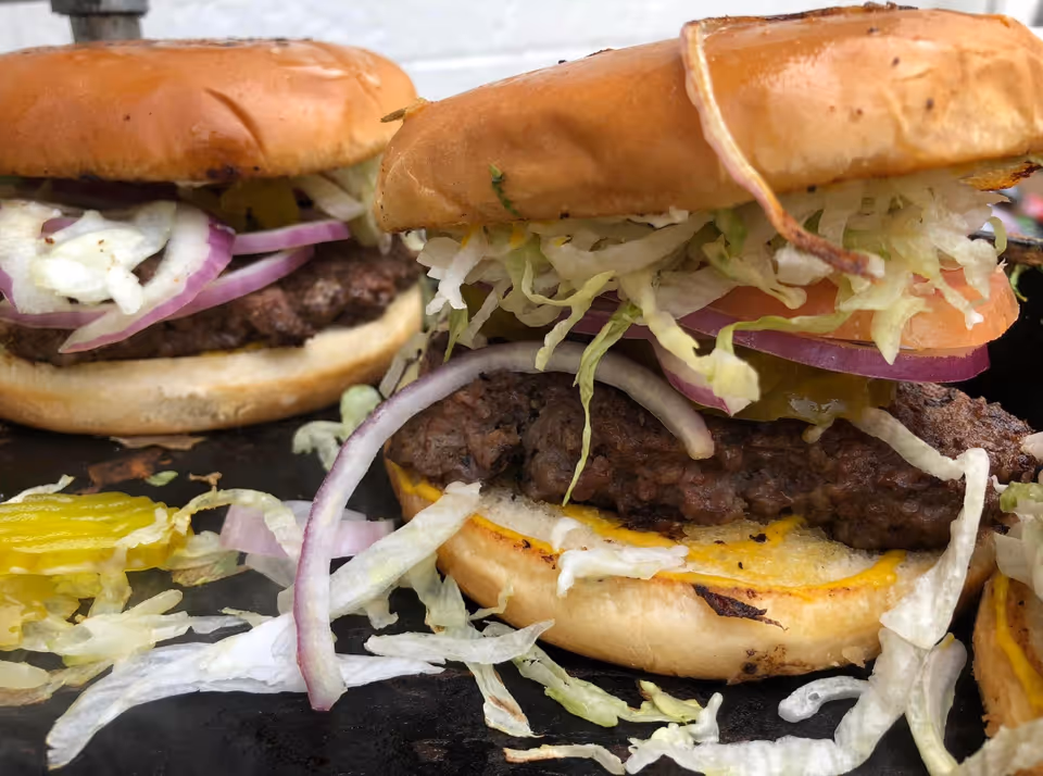 Close-up of two cheeseburgers with shredded lettuce, red onion, pickles and toasted buns.