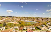 Aerial view of a suburban neighborhood with houses, trees, and a sports field under a blue sky with scattered clouds.