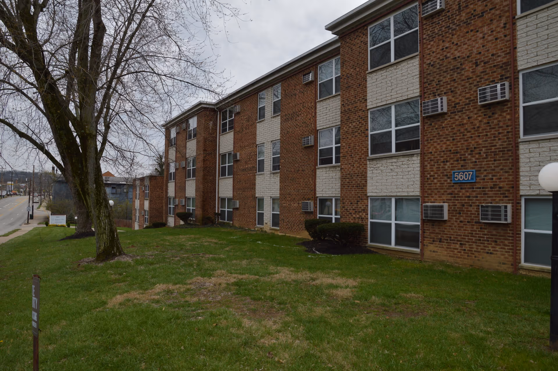 Brick three-story residential building with a grassy front lawn, trees, and visible address number 5607.