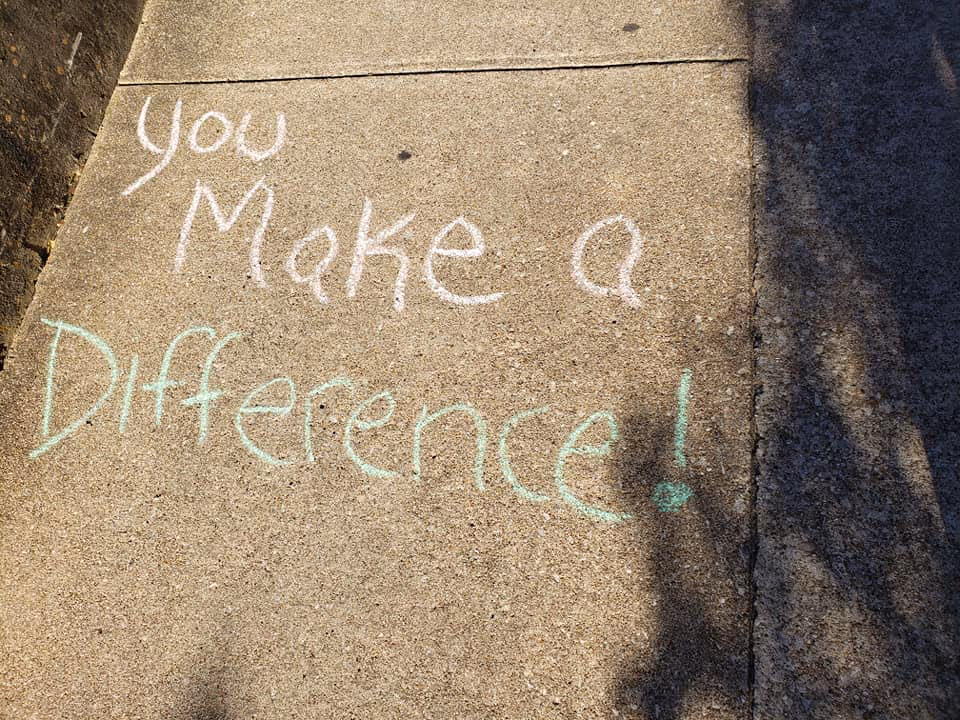 Concrete sidewalk with chalk writing that reads "You Make a Difference!" and tree shadows.