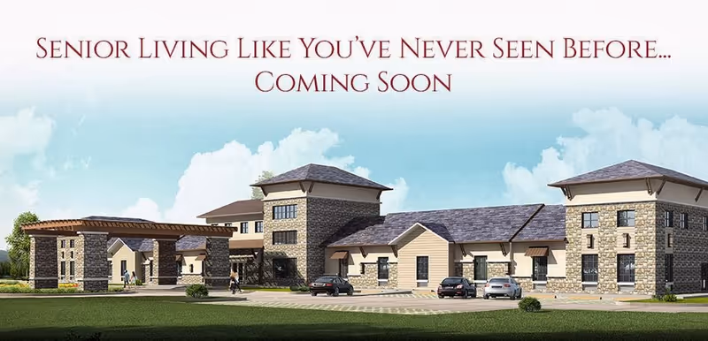Rendering of a senior living facility building with stone and beige siding, multiple roof levels, and a covered entrance. Several cars are parked in front, and a few people are walking near the entrance. The sky is blue with some clouds.