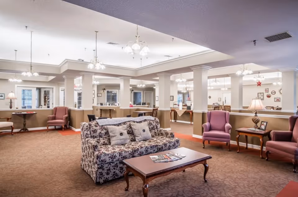 Spacious senior living lounge with sofas, armchairs, tables, and chandeliers.