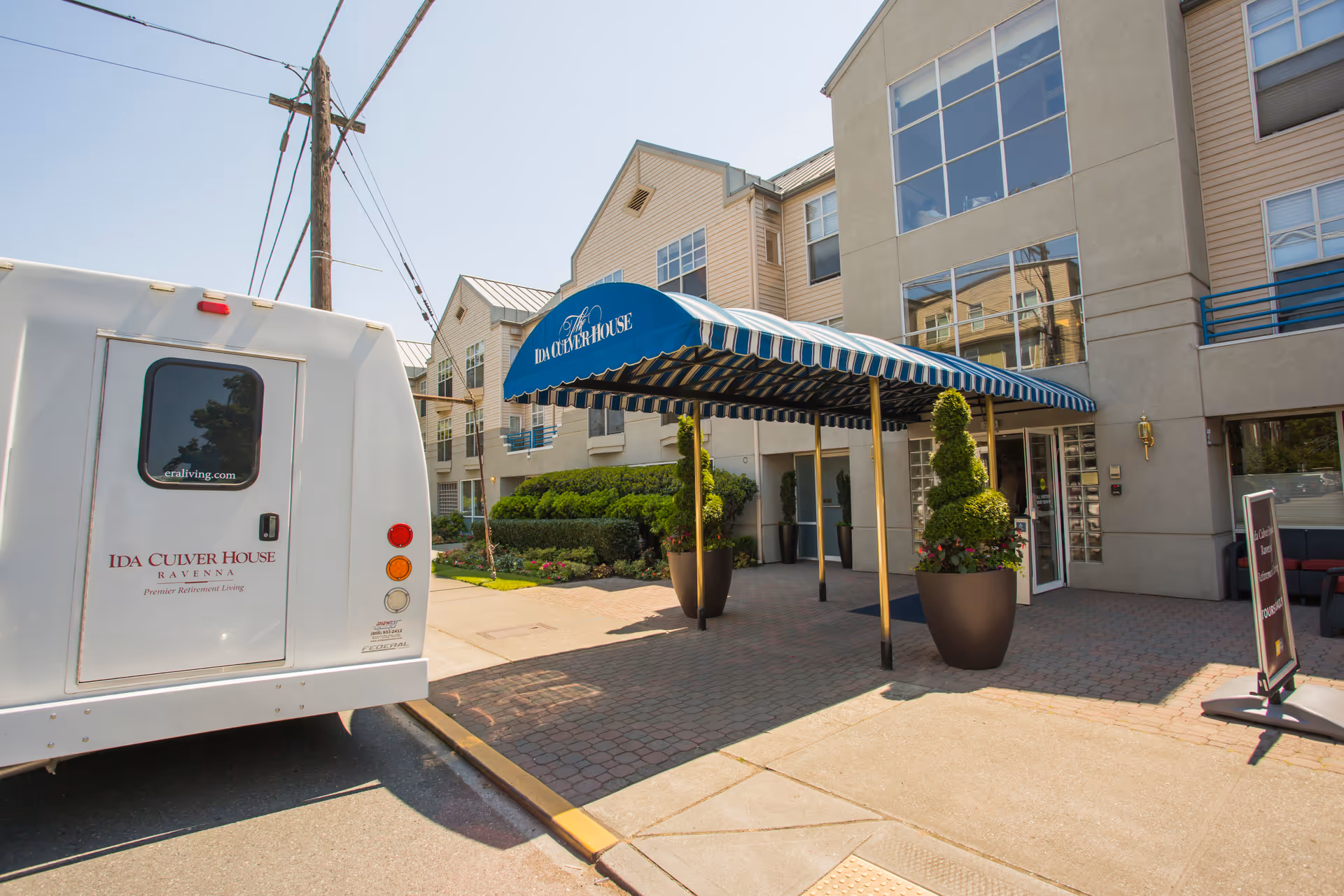 Entrance of Ida Culver House Ravenna with a blue striped awning and a facility shuttle parked to the left.
