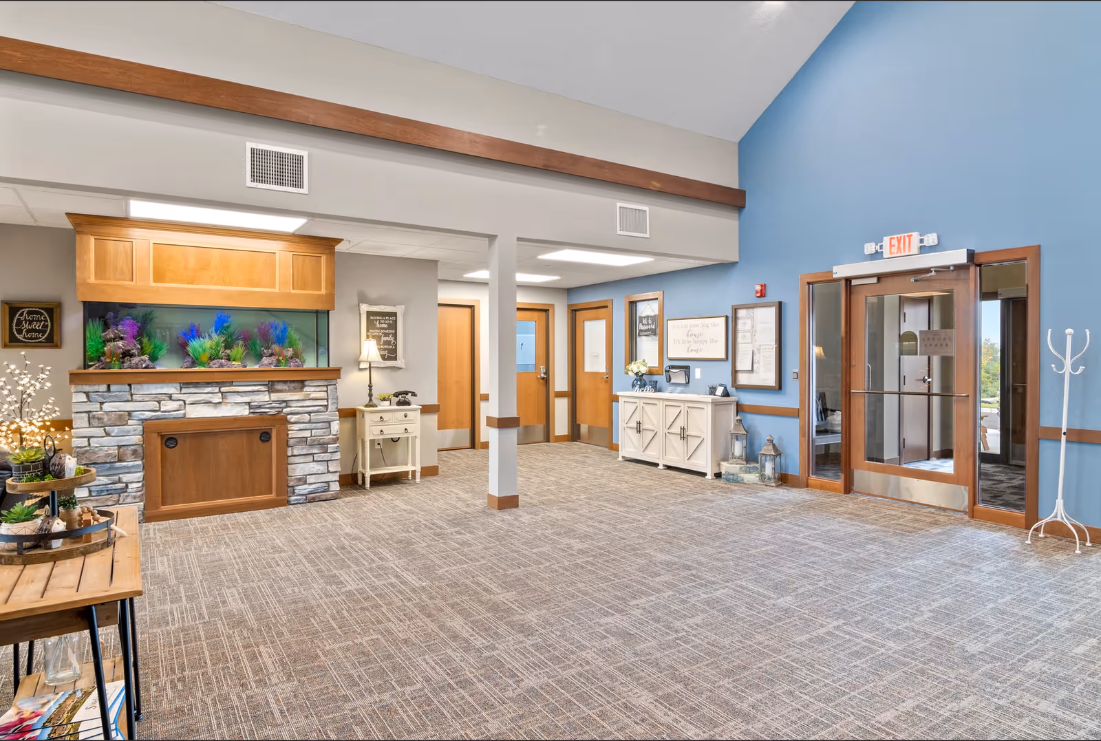 Spacious senior living facility lobby with a large decorative aquarium in a stone mantle, reception furniture, and glass exit doors.