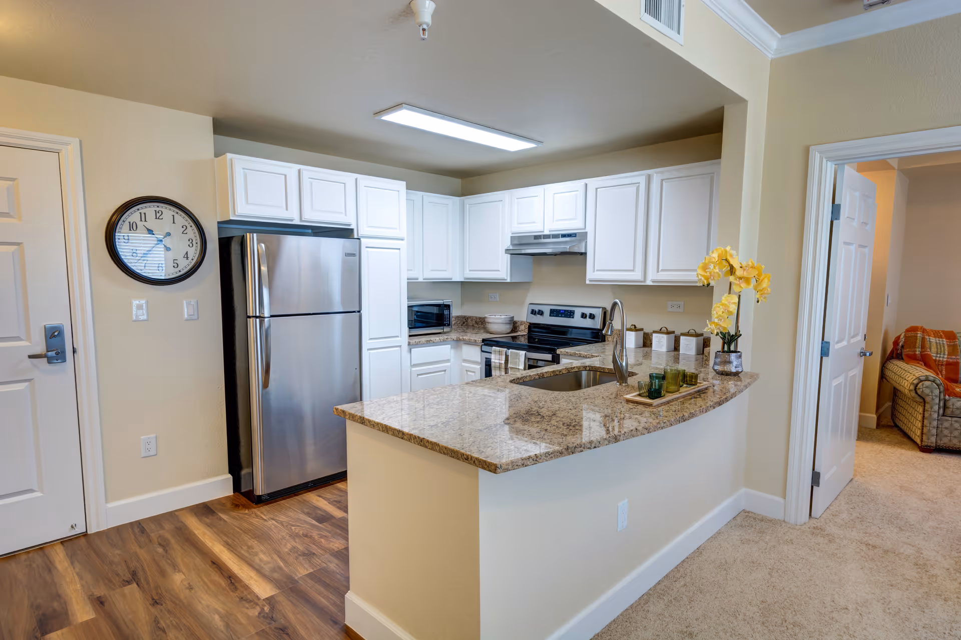 Open kitchen with a granite countertop island, stainless steel refrigerator, white cabinets, and a view into the adjacent living area.