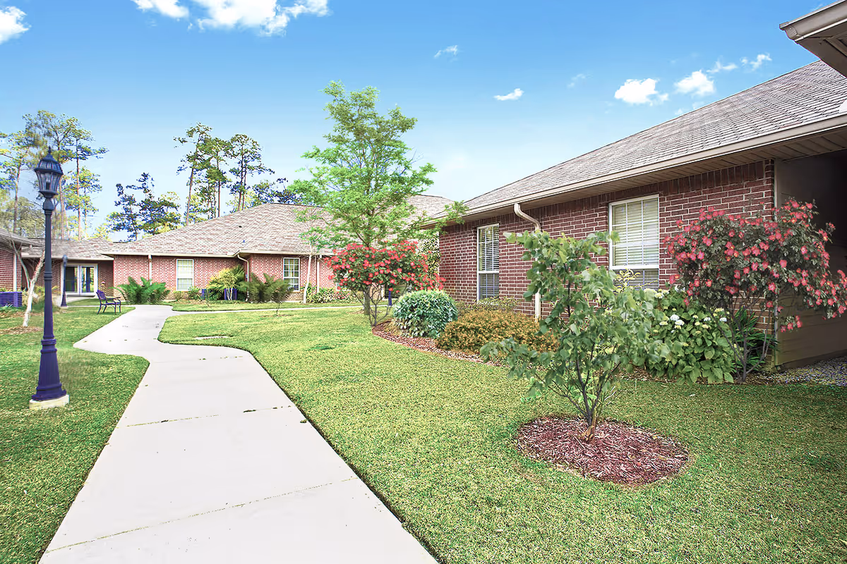 Single-story brick senior living buildings surrounding a landscaped courtyard with a concrete walkway and lamppost.