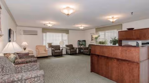 Interior lounge area with multiple chairs, a reception desk, lamps, and plants.