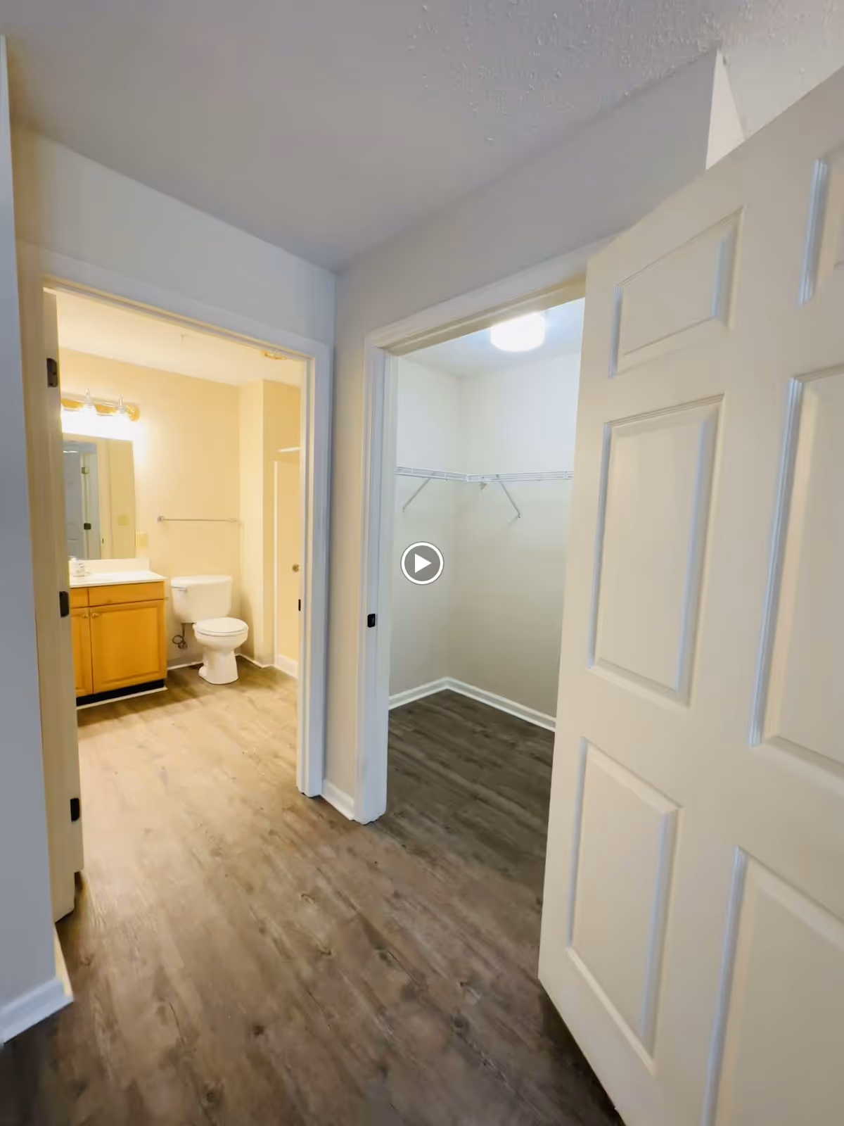 Hallway showing an open bathroom with a vanity and toilet on the left and an empty walk-in closet on the right.