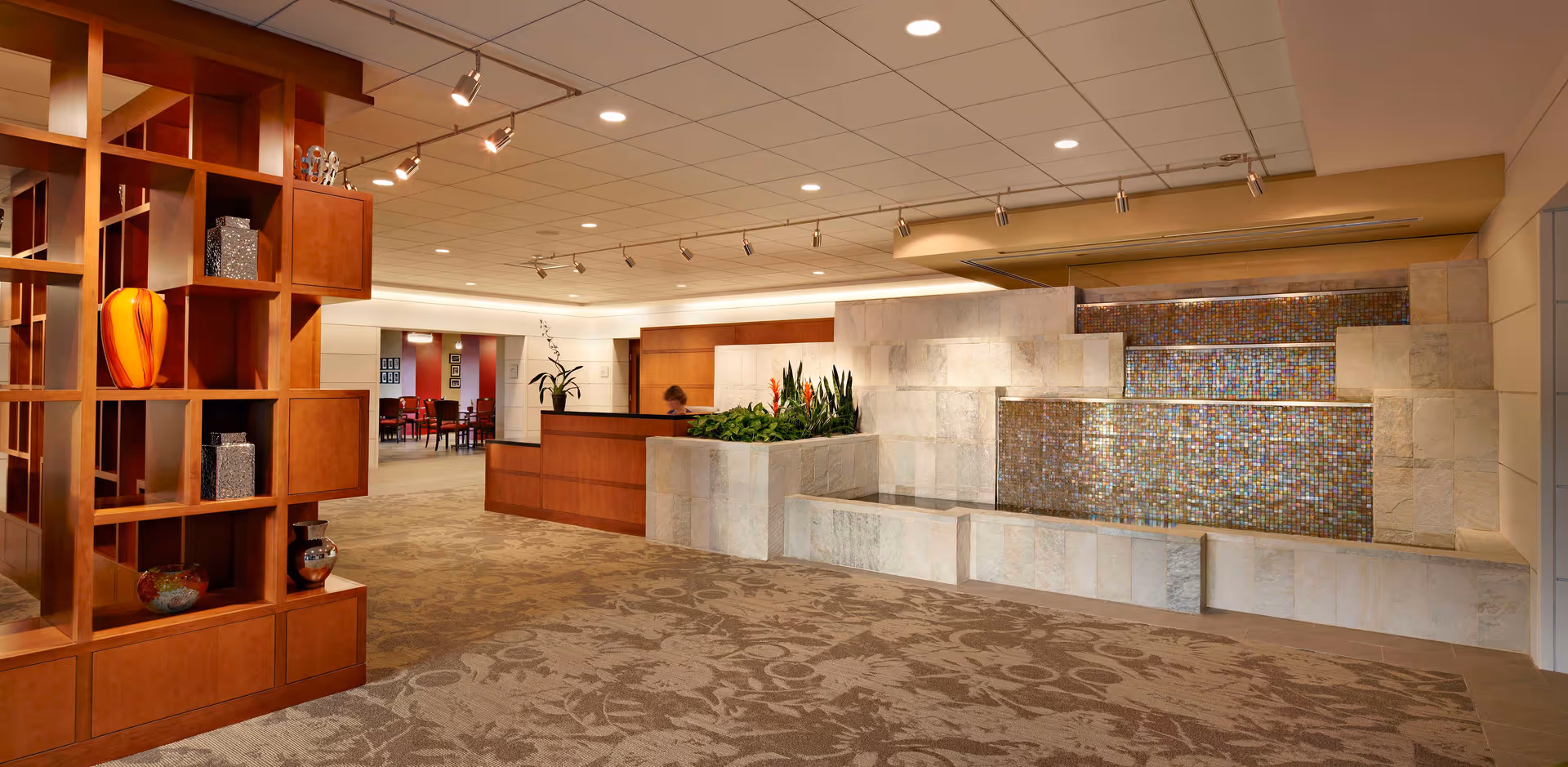 Spacious interior lobby with a reception desk, decorative wooden shelving, and a tiled cascading water feature.
