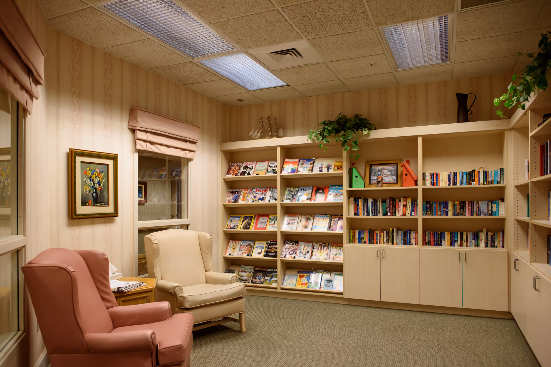 Cozy reading room with two armchairs, framed art, bookshelves and a magazine rack.