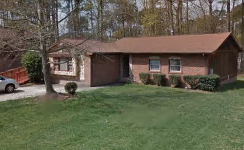 Single-story brick senior living building with a grassy front yard and surrounding trees.