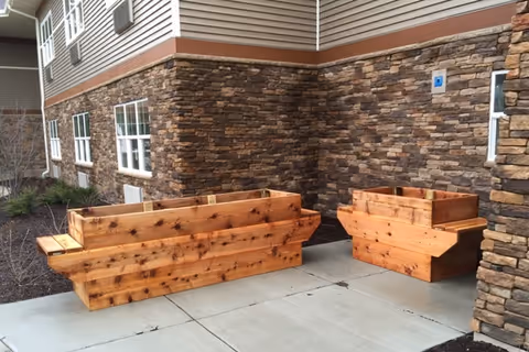 Two wooden planter boxes placed on a concrete patio area next to a building with stone and siding exterior walls.