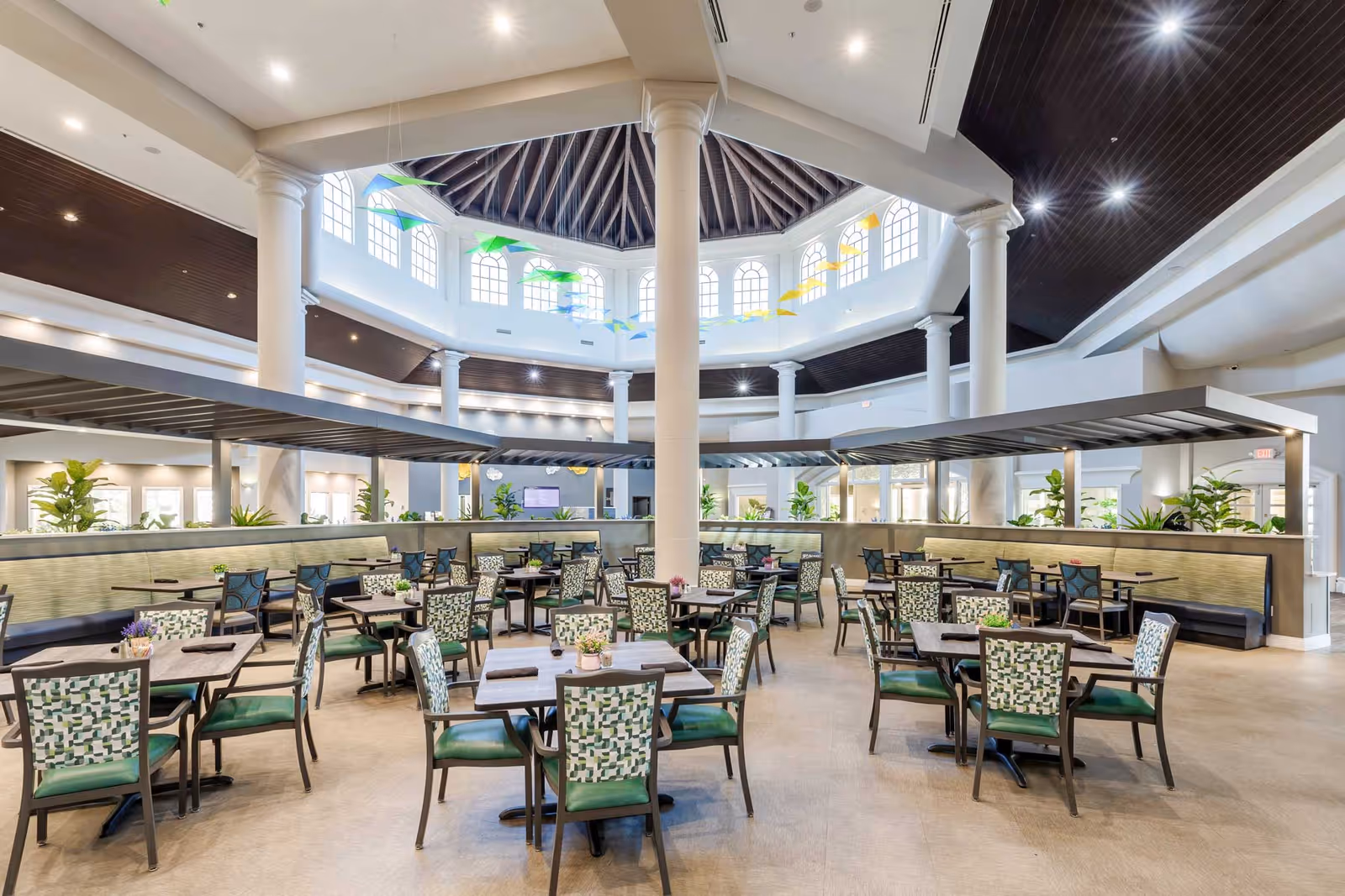 Spacious, well-lit dining room with multiple tables and patterned chairs beneath a large central skylight and columns.