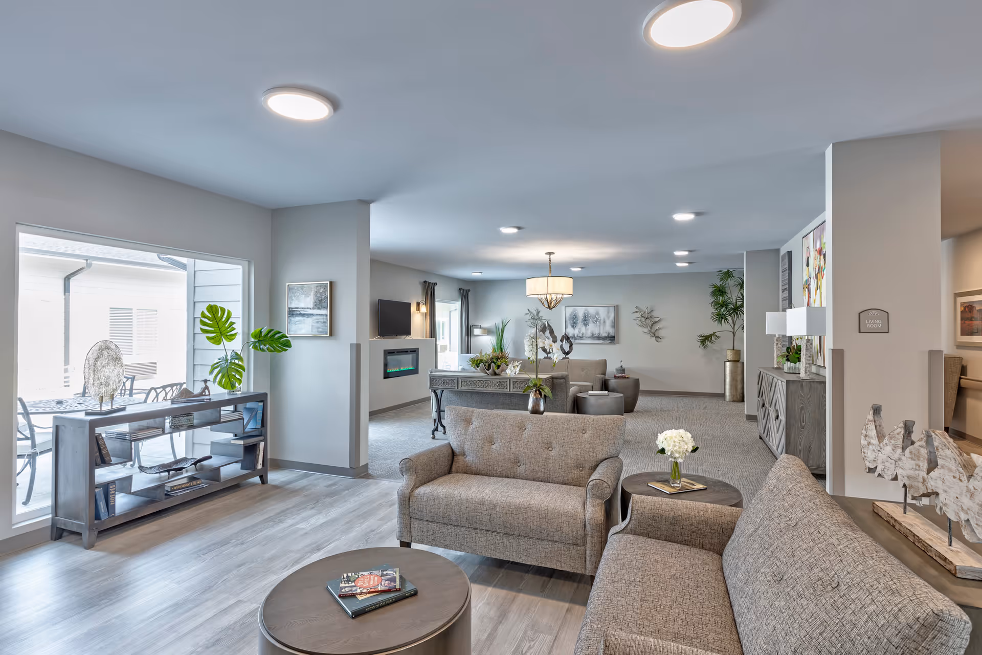 Spacious bright communal living room with sofas, coffee tables, decorative plants and a view to an outdoor patio.