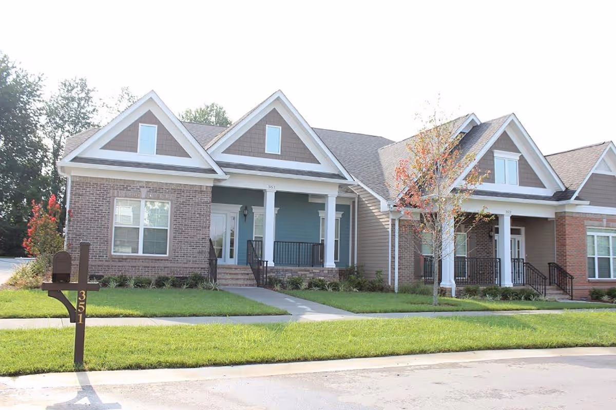 Exterior view of a single-story residential building with brick and siding facade, featuring two front porches with white columns, a mailbox with the number 351, a small tree, and a well-maintained lawn.