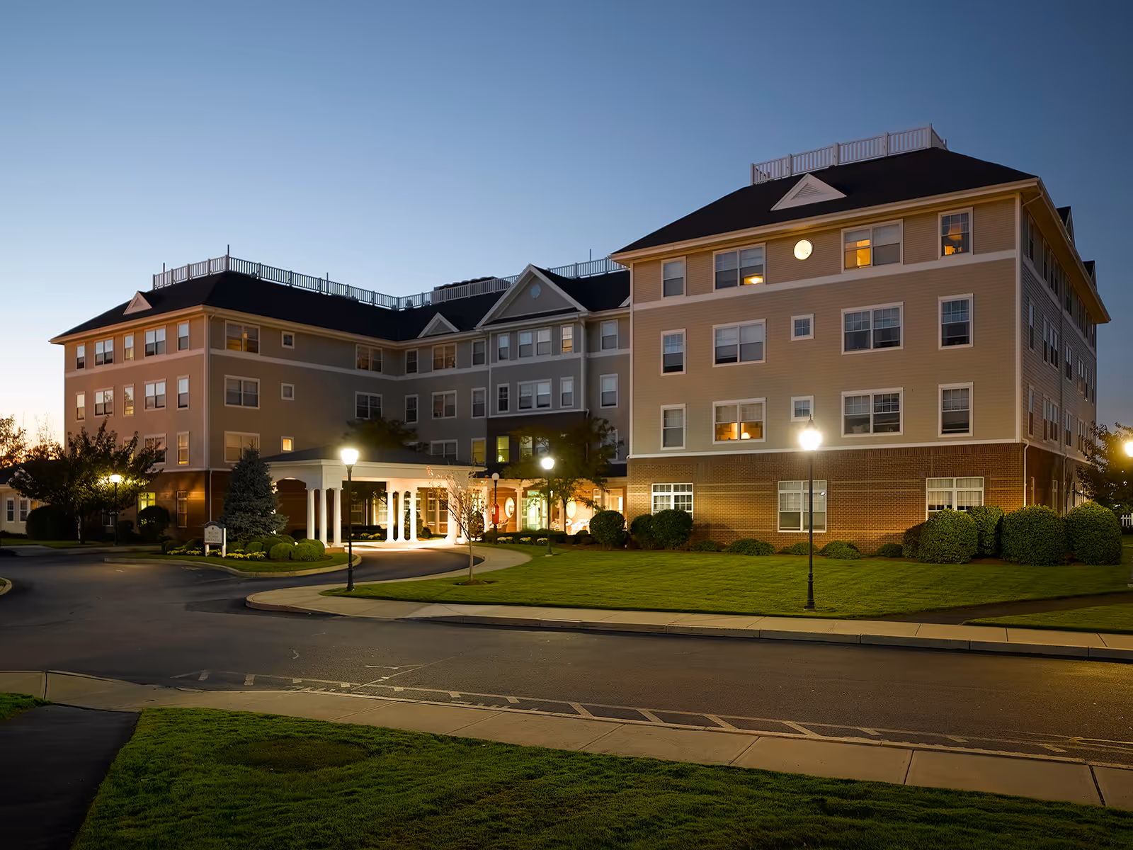 An exterior view of a multi-story senior living building at dusk with landscaped grounds.