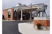 Front entrance of a brick nursing and rehab building with a covered porte-cochère and a large horse statue on a brick pedestal.