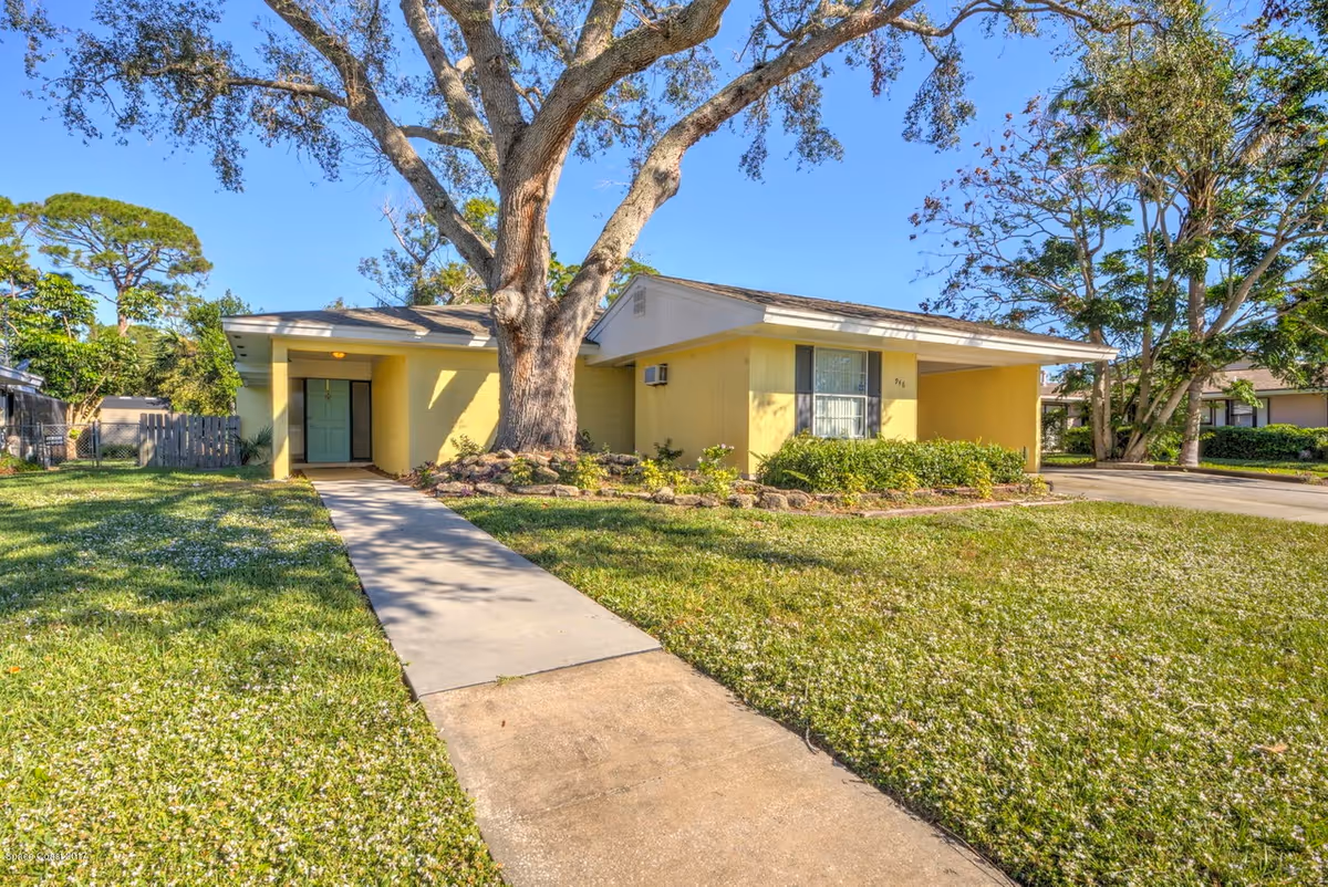 Yellow single-story assisted living facility with a large tree, walkway, and manicured lawn.