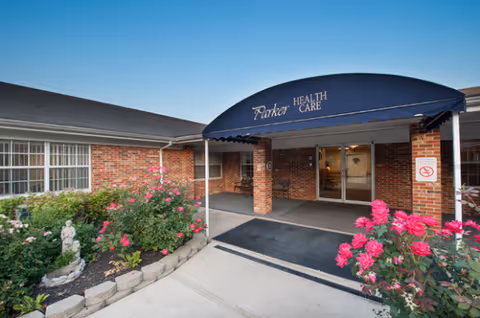Exterior view of Parker Health and Rehabilitation Center entrance with a blue canopy and blooming flowers.