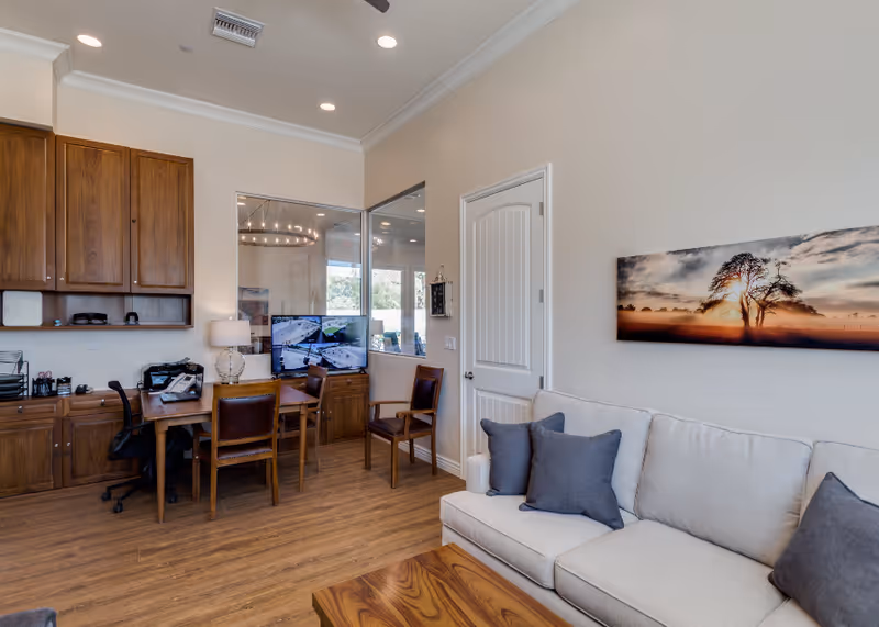 Interior common area with wooden cabinets, desk, monitor, chairs, and beige sofa.
