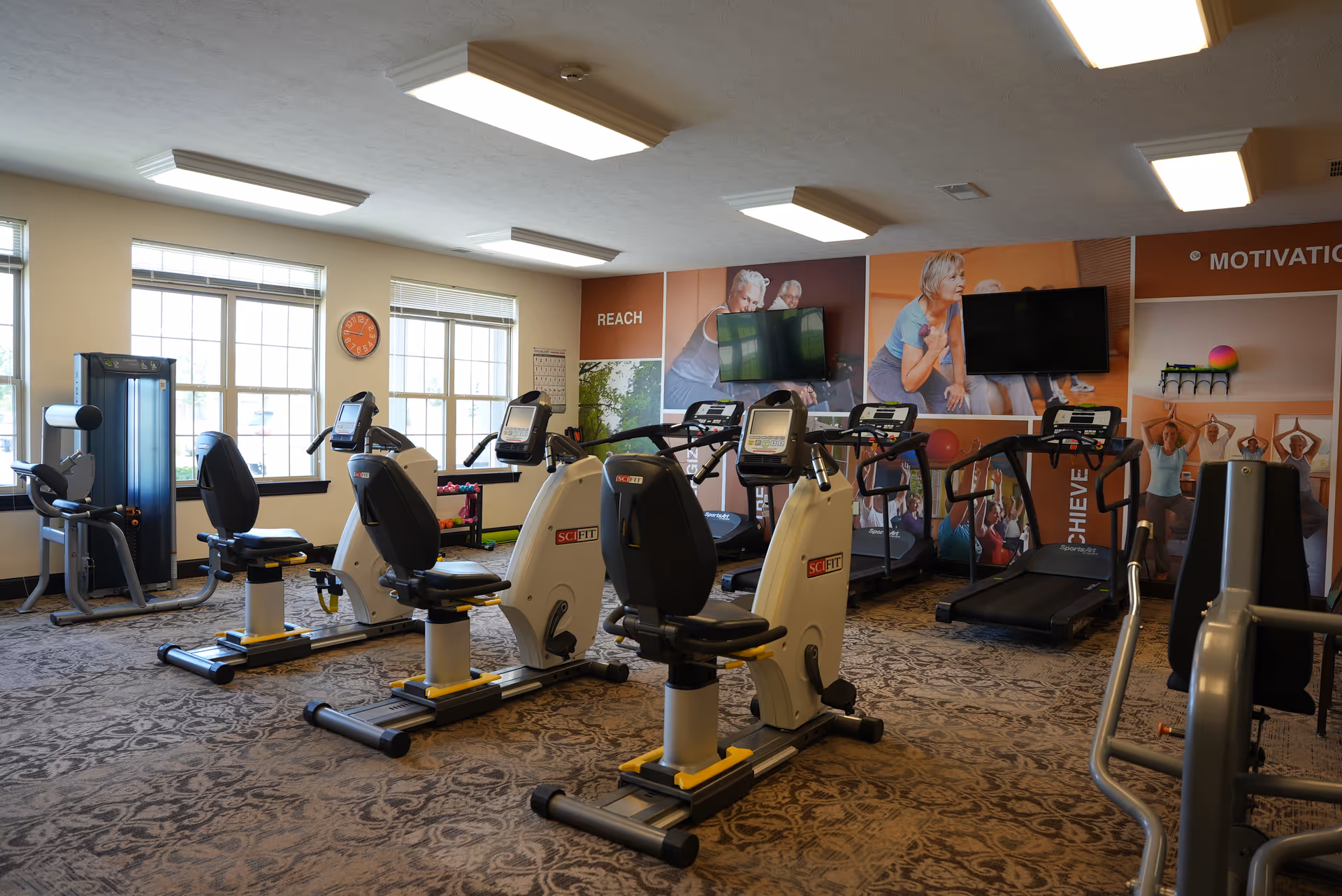 Exercise room with recumbent bikes, treadmills, weight machines, TVs and motivational wall murals.