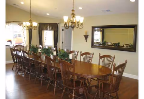 A long wooden dining table with chairs, chandeliers, and plants in a well-lit dining room.