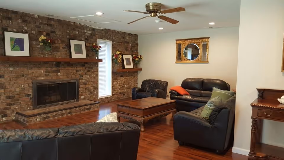 Spacious living room with a brick fireplace, leather sofas, a wooden coffee table, and a ceiling fan.