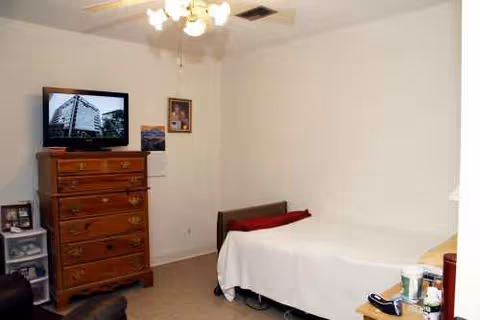A bedroom in a senior residence with a bed, dresser, and TV.