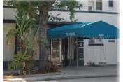 Entrance to a building with a blue awning that has the name 'Wirick' and the number '434' on it. There are plants and a tree near the entrance, and the building exterior is white with windows.