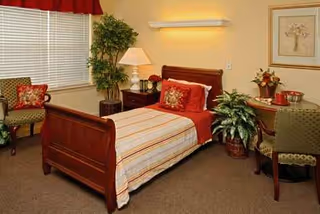 A bedroom in a senior living facility featuring a wooden bed, striped bedding, and plants.