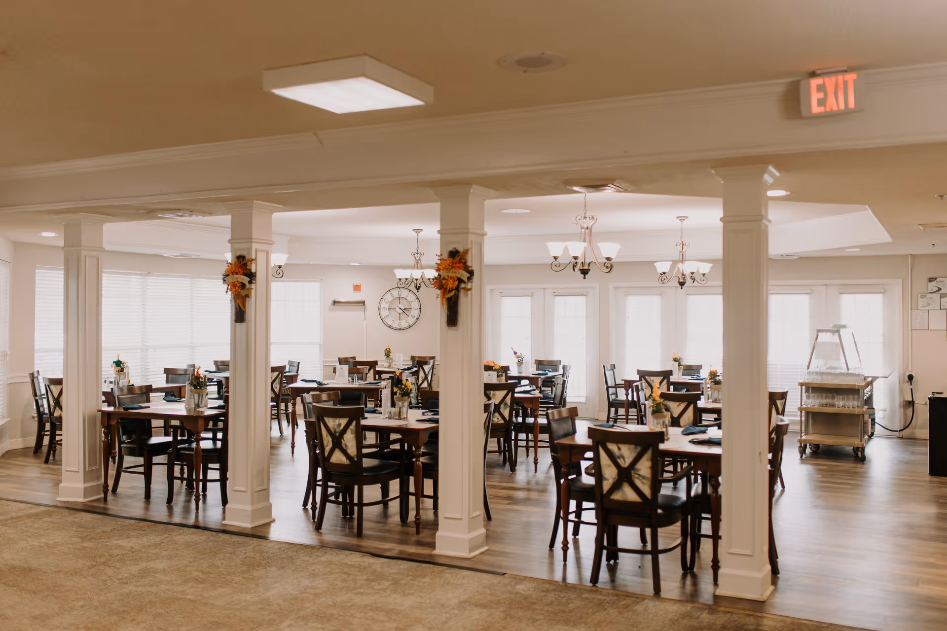 Spacious dining room with multiple tables and chairs, chandeliers, decorative columns, and place settings.