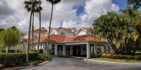 Exterior view of Princeton Village of Largo with red-roofed entrance and palm trees.