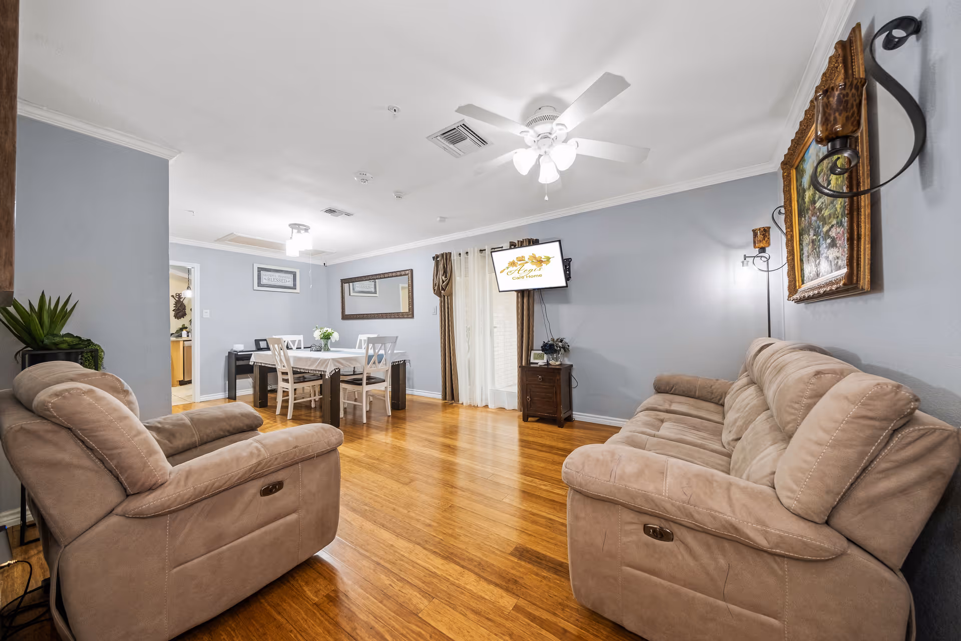Open living area with two beige recliner sofas facing a wall-mounted TV and a dining table in the background.