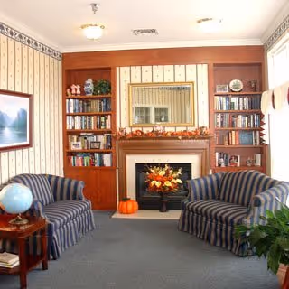 Cozy sitting room with two striped armchairs facing a fireplace flanked by built-in bookshelves and a mirror above the mantel.