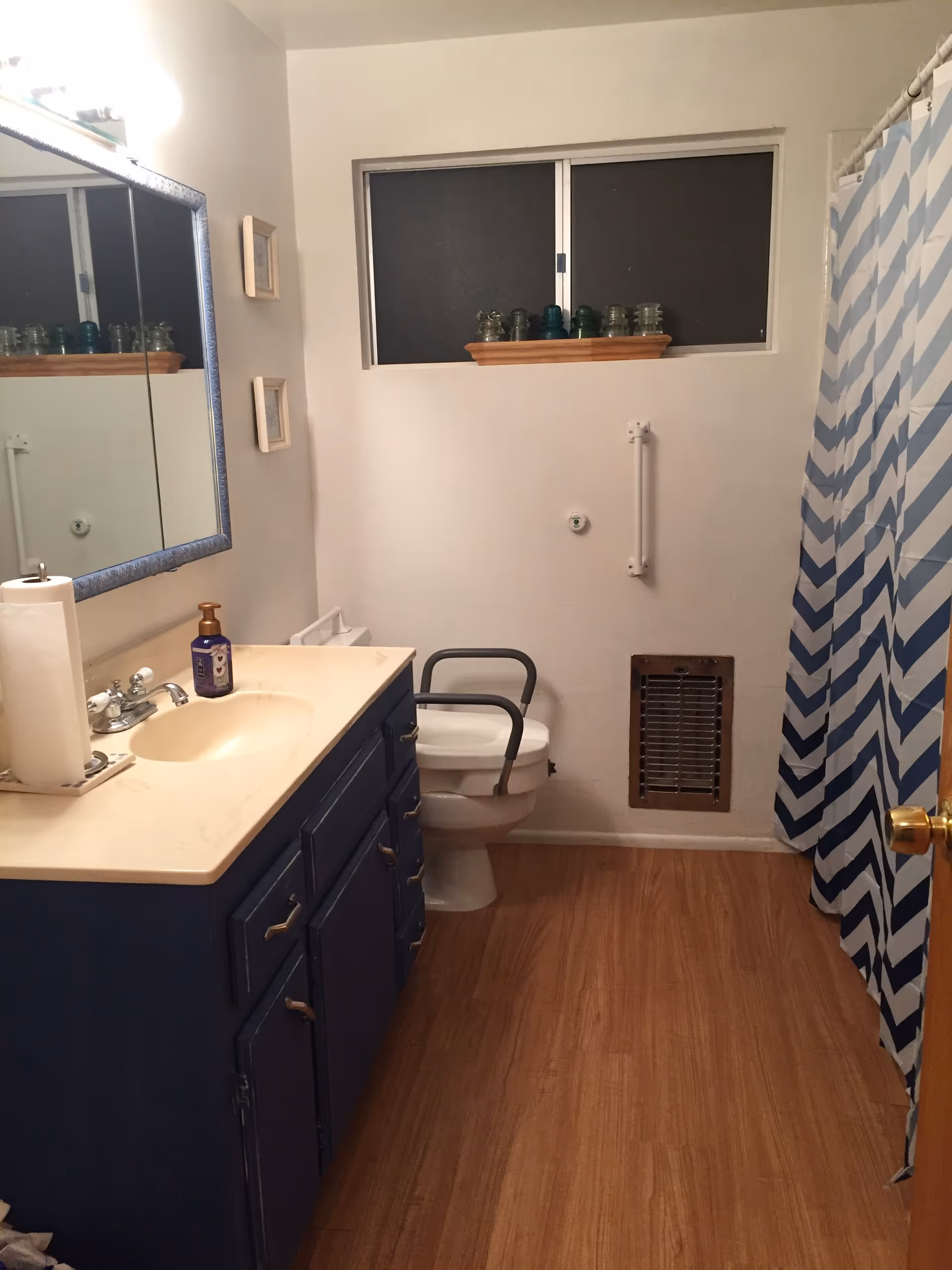 Bathroom featuring a blue vanity and sink, a toilet with safety armrests, and a blue chevron shower curtain.