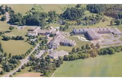 Aerial view of a senior living campus with multiple connected buildings, driveways, lawns, and surrounding trees and fields.