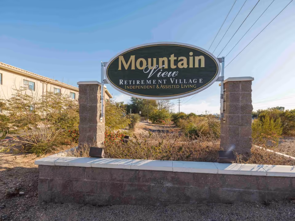 Outdoor view of the entrance sign for Mountain View Retirement Village, an independent and assisted living facility, with landscaping and a building visible in the background under a clear blue sky.