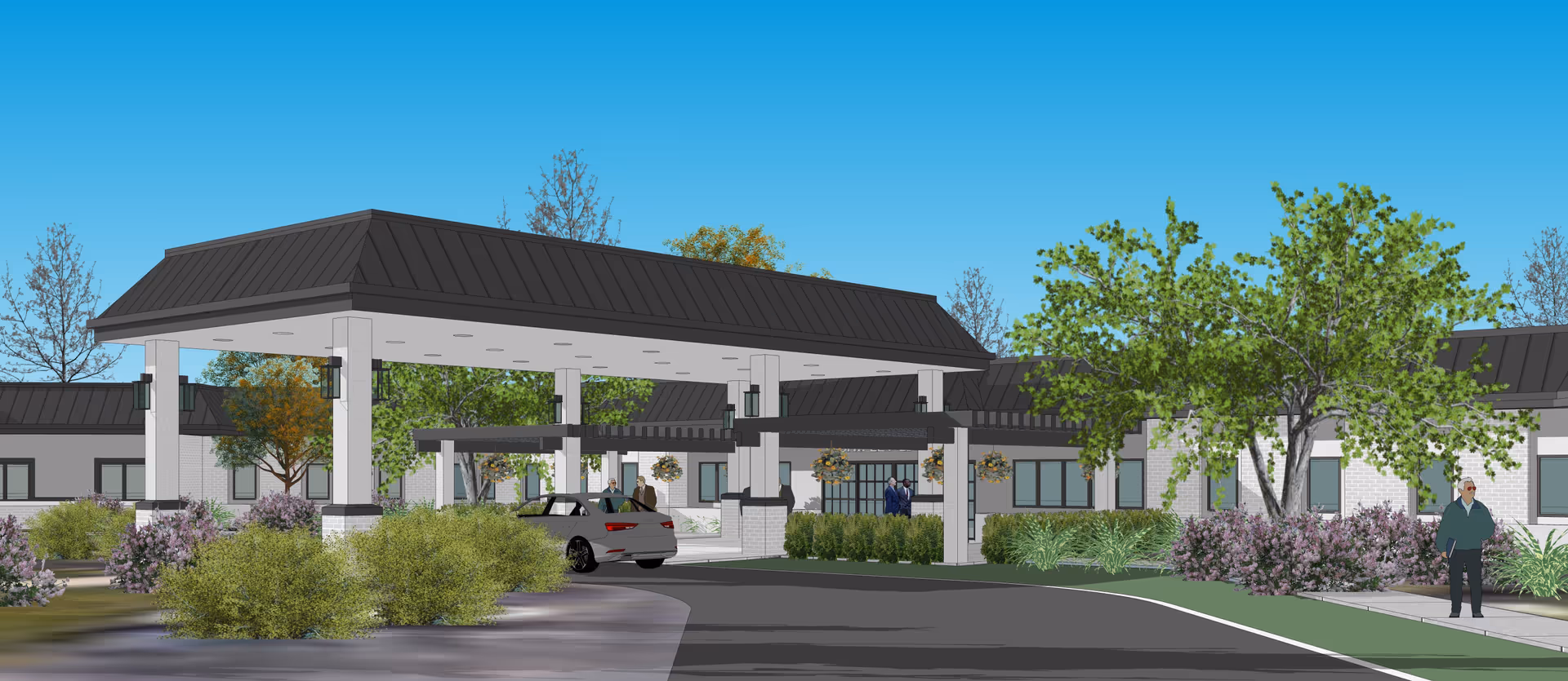 Exterior view of a senior living facility entrance with a covered drop-off area, surrounded by landscaping including trees and bushes. Several people are visible near the entrance and on the sidewalk. The building has a modern design with a dark roof and light-colored walls under a clear blue sky.