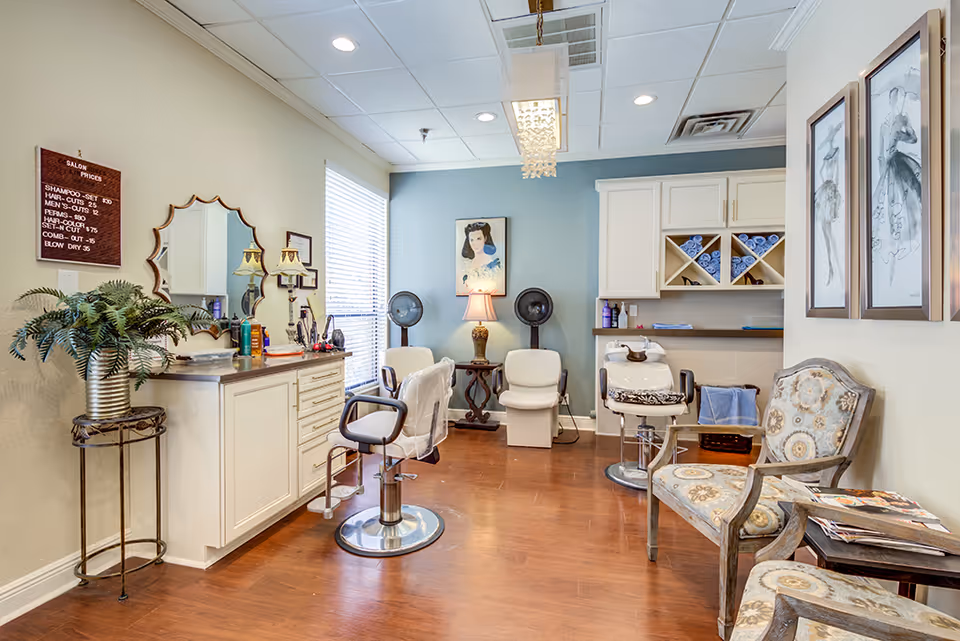 Bright salon room with styling chairs, hair-washing stations, cabinets, and decorative seating in a retirement community.