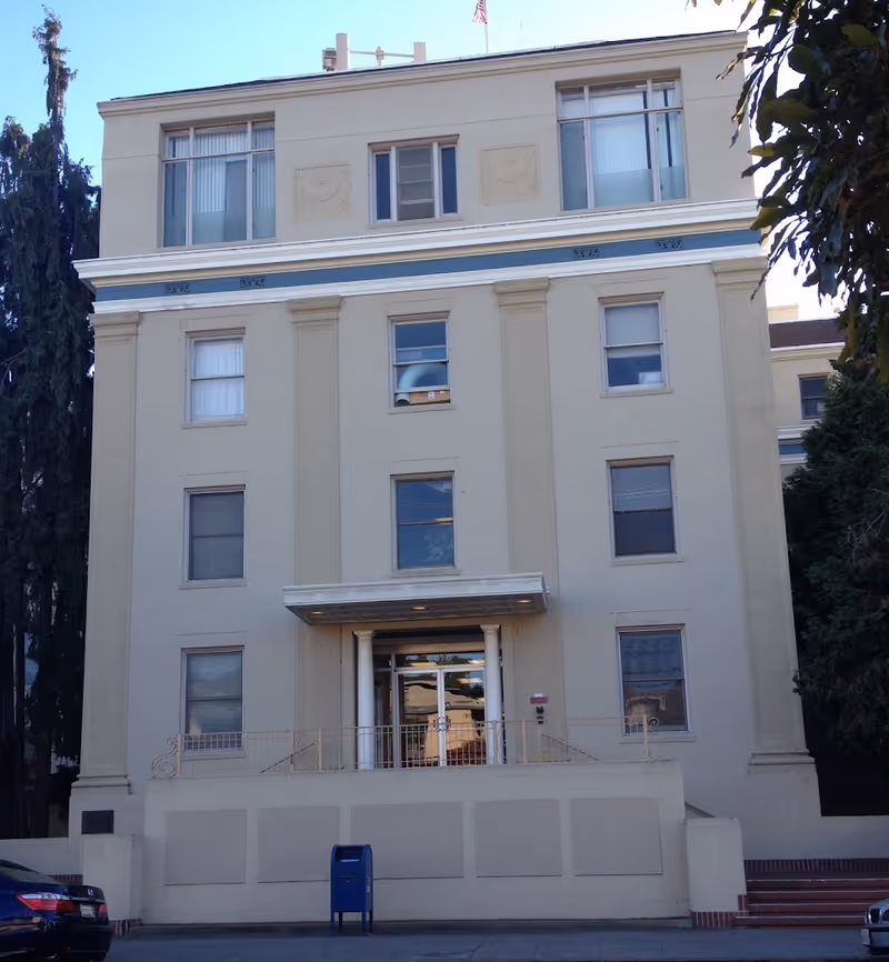Front facade of a four-story beige institutional building with columns and a covered entrance.