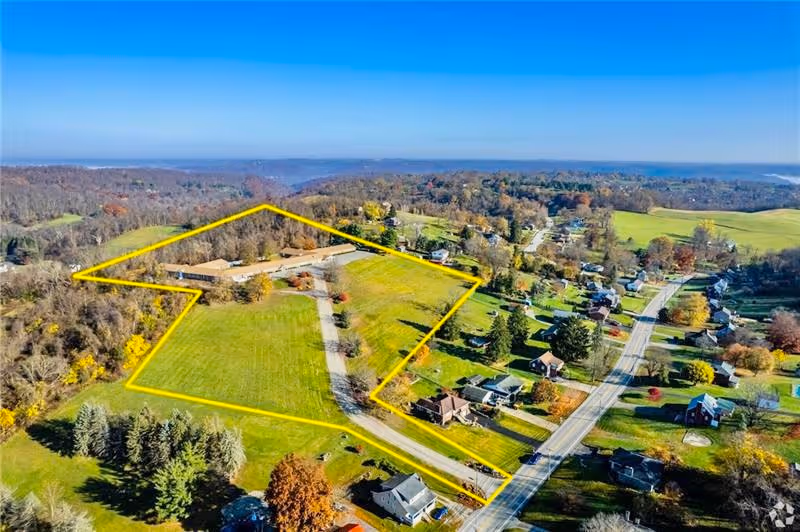 Aerial view of a rural property and nearby homes with the facility buildings and grounds outlined in yellow.