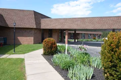 Brick facility with a covered entrance and landscaped walkway along a sidewalk.